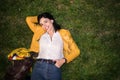 Happy young woman smiling and lying on green grass wearing colorful outfit with yellow jacket and blue jeans at night Royalty Free Stock Photo