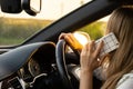 Happy young woman speaking by mobile phone while driving car. Business woman talking phone call in automobile. Unsafely