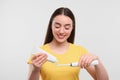 Happy young woman squeezing toothpaste from tube onto electric toothbrush on white background Royalty Free Stock Photo