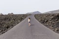 Happy young woman standing in the middle of a road in volcanic scenery in Lanzarote, Canary Islands