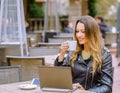 Happy young woman in stylish outfit smiling in outdoor cafe and browsing modern