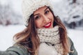 Happy young woman takes selfie in snowy winter park wearing warm knitted clothes and red festive lipstick. Royalty Free Stock Photo