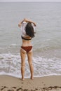 Happy young woman taking off wet white shirt on beach, back view. Stylish girl in swimsuit relaxing on seashore. Summer vacation. Royalty Free Stock Photo