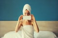 Happy young woman taking selfie with phone drying her wet hair after bath with wrapped towel on her head sitting on bed in the Royalty Free Stock Photo