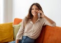Happy young woman talking on cellphone while sitting on sofa at home Royalty Free Stock Photo