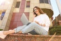 Happy young woman talking on phone while using laptop outdoors, low angle view Royalty Free Stock Photo