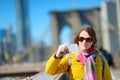Happy young woman tourist sightseeing at Brooklyn Bridge, New York City, at sunny spring day. Female traveler enjoying view of dow Royalty Free Stock Photo