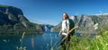 Happy young woman travels with a backpack in Norway, stands on a mountain with a beautiful landscape view from the Norwegian