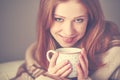 Happy young woman is under a blanket and cup of coffee on winter morning at home Royalty Free Stock Photo