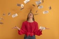 Happy young woman under money rain on orange background. Girl throwing money. Big profit or win lottery concept Royalty Free Stock Photo