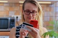 Happy young woman using credit card and phone in kitchen at home Royalty Free Stock Photo