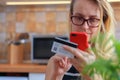 Happy young woman using credit card and phone in kitchen at home Royalty Free Stock Photo