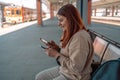 Happy young woman waiting on station platform with backpack on background train using smart phone. Railroad transport Royalty Free Stock Photo