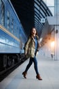 Happy young woman waitng train on the railway station platform. Woman travel with the train.