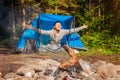 Happy young woman waking up in tent by campfire in summer forest. Traveler raising arms feeling good camping. Royalty Free Stock Photo