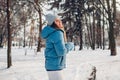 Happy young woman walking in snowy winter park wearing blue coat. Girl enjoys landscape wearing hat and mittens Royalty Free Stock Photo