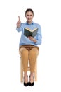 Happy young woman holding book and making thumbs up sign Royalty Free Stock Photo