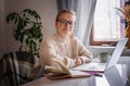 Happy young woman wearing glasses sitting at home and using laptop, online work and education concept Royalty Free Stock Photo