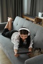 Happy woman wearing headphone and using digital tablet while lying on sofa. Royalty Free Stock Photo