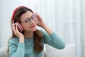 Happy young woman wearing headphones listening music while sitting on sofa with fun and enjoy in the living room. Royalty Free Stock Photo