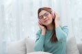 Happy young woman wearing headphones listening music while sitting on sofa with fun and enjoy in the living room. Royalty Free Stock Photo