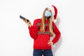 Happy young woman, wearing red santa claus hat and medical protective mask on face, with mobile phone, isolated on white Royalty Free Stock Photo