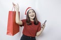 A happy young woman wearing Santa Claus` hat is smiling while holding Christmas presents and her smartphone Royalty Free Stock Photo