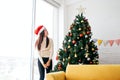 Happy young woman wearing a Santa Claus hat and sweater, smile and enjoy decorating various baubles on the Christmas tree. Royalty Free Stock Photo