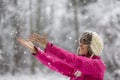 Happy young woman wearing warm hat and bright pink jacket standing outside in snowy nature