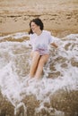 Happy young woman in wet white shirt lying on beach in splashing waves.  Emotional tanned girl relaxing on seashore and enjoying Royalty Free Stock Photo