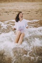 Happy young woman in wet white shirt lying on beach in splashing waves.  Emotional tanned girl relaxing on seashore and enjoying Royalty Free Stock Photo