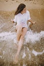 Happy young woman in wet white shirt lying on beach in splashing waves. Top view. Emotional tanned girl relaxing on seashore and Royalty Free Stock Photo