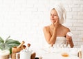 Happy young woman in white bathtowels applying creme on her face skin doing spa precedures Royalty Free Stock Photo