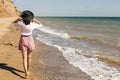 Happy young woman in white shirt and hat walking on sunny beach. Hipster slim girl relaxing near sea with waves, sunny warm Royalty Free Stock Photo