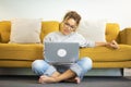 Happy young woman working on laptop sitting on floor against sofa in living room at home. Businesswoman in casuals working from Royalty Free Stock Photo