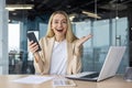 A happy young woman is working in the office at a table with a laptop and holding a mobile phone in her hands Royalty Free Stock Photo