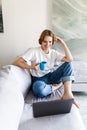 Young woman works on the laptop with cup of coffee on a sofa Royalty Free Stock Photo