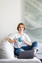 Young woman works on the laptop with cup of coffee on a sofa Royalty Free Stock Photo