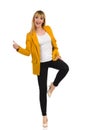 Happy Young Woman In Yellow Jacket Is Standing On One Leg And Showing Thumb Up Royalty Free Stock Photo