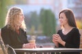 Happy young women friends drinking coffee at city street restaurant during work break. Socializing and friendship Royalty Free Stock Photo