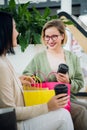 Happy young women with shopping bags and coffee paper cups sitting, resting and talking after shopping in mall Royalty Free Stock Photo