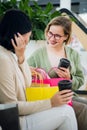 Happy young women with shopping bags and coffee paper cups sitting, resting and talking after shopping in mall Royalty Free Stock Photo