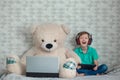 Happykid in headphones playing on digital tablet next to a toy bear looking at a computer