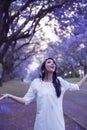 Happyl woman in white dress standing in street surrounded by purple falling Jacaranda blooms Royalty Free Stock Photo
