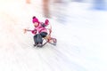 Hapy cutee litlle girl having fun sledging from hill on bright sunny day. Child moving fast on sledges downhill at Royalty Free Stock Photo