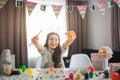 Hapy positive girl prepare for Easter alone. She sit at table in room and painting eggs. Girl hold brush and egg. Smile