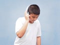 Happy asian boy with white shirt wearing headphone and listening to music over blue wall background. Royalty Free Stock Photo