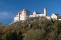 The Harburg castle stands high on a hill with forest. The trees are slightly discolored in autumn. The sky is blue. The sun