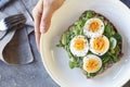 Hard boiled egg on avocado toast with green leaves, healthy breakfast or lunch, top view, man`s hand holding a plate