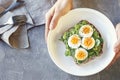 Hard boiled egg on avocado toast with green leaves, healthy breakfast or lunch, top view, man`s hands holding a plate, grey backg